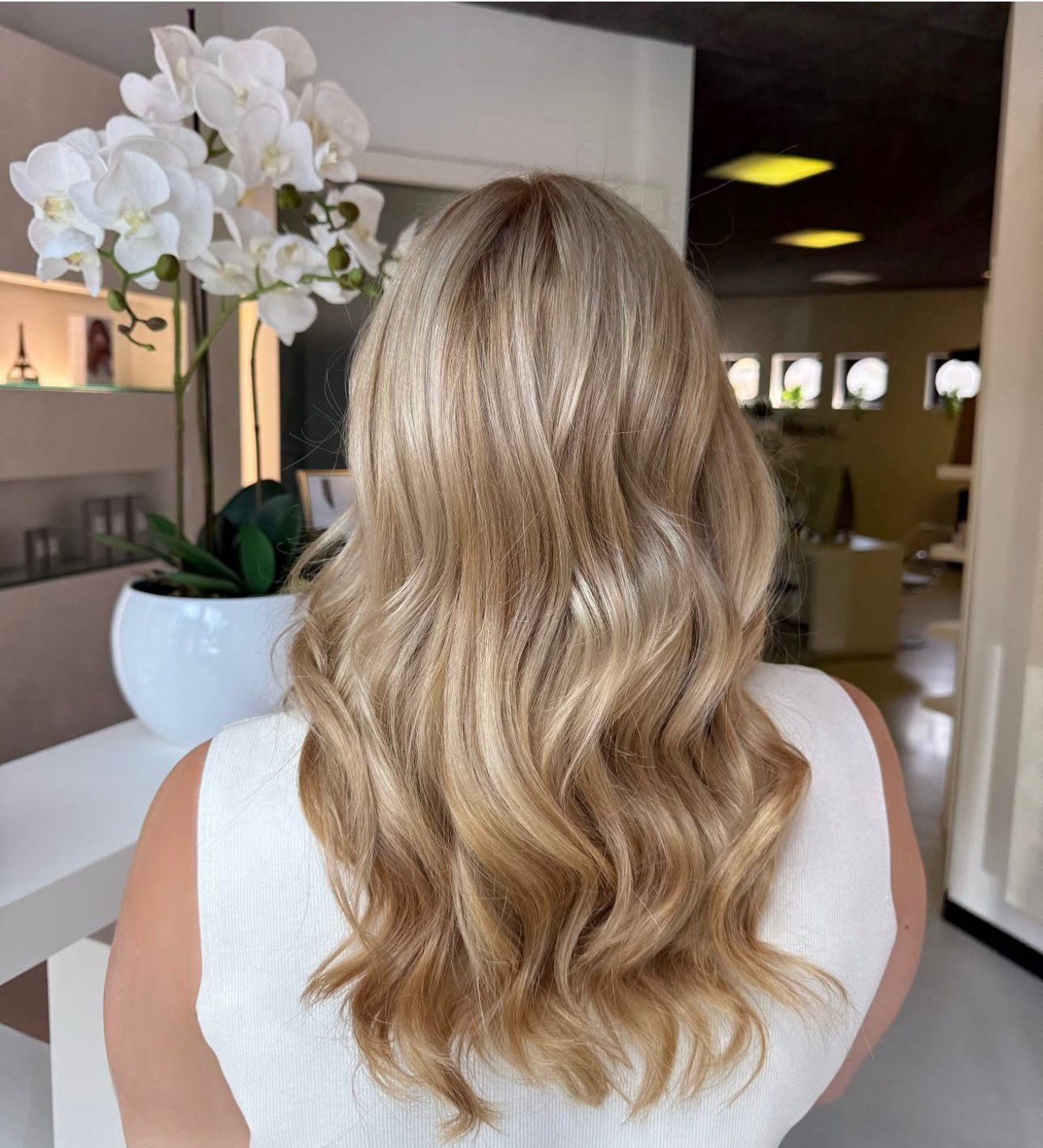 Una donna con lunghi capelli scuri e ondulati, che indossa una camicetta bianca, è in piedi in un salone.