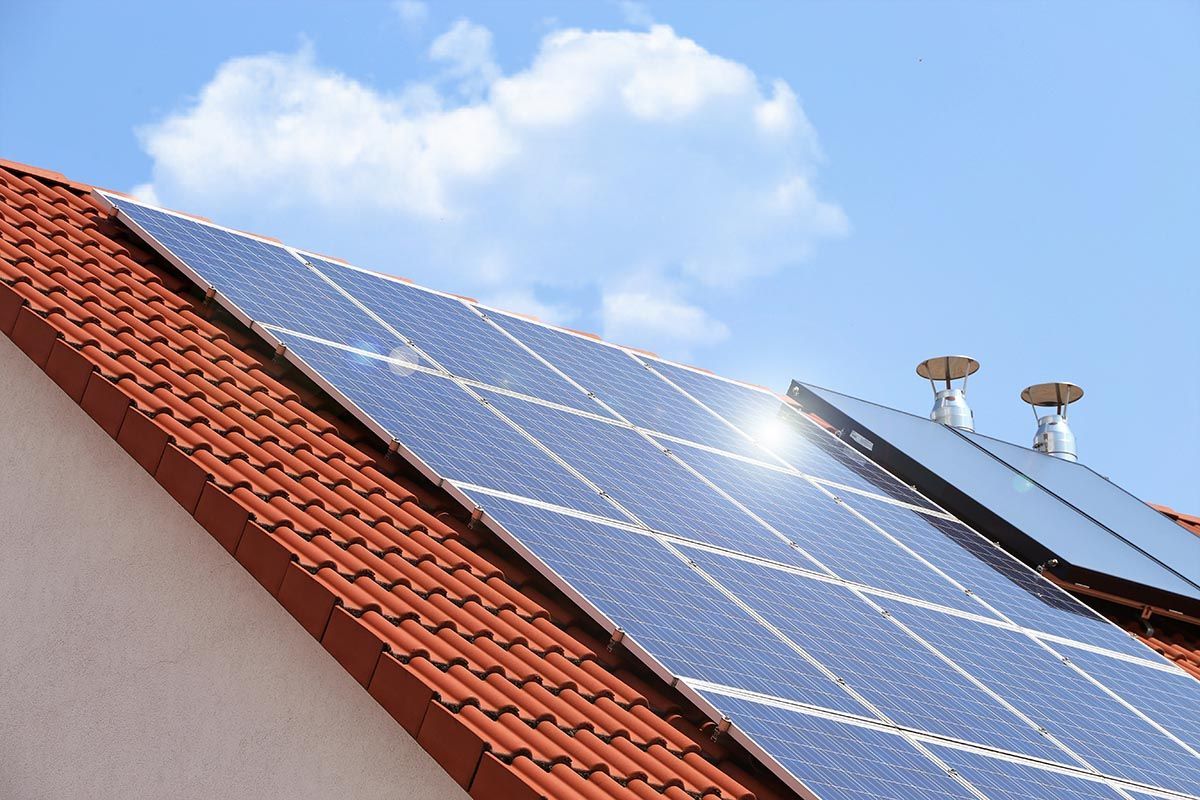 Solarpaneele auf einem schrägen, rot gedeckten Ziegeldach unter blauem Himmel mit Wolken