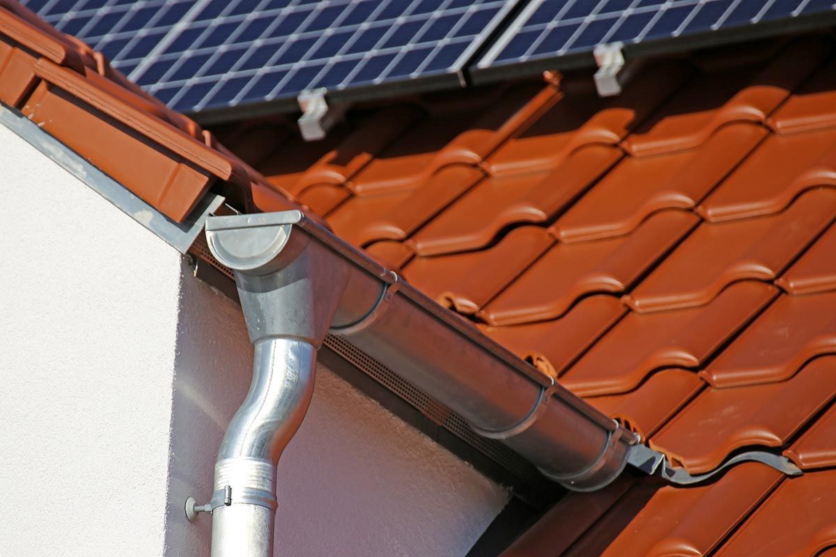 Dachrinne und Fallrohr auf einem roten Ziegeldach mit darüberliegenden Solarmodulen