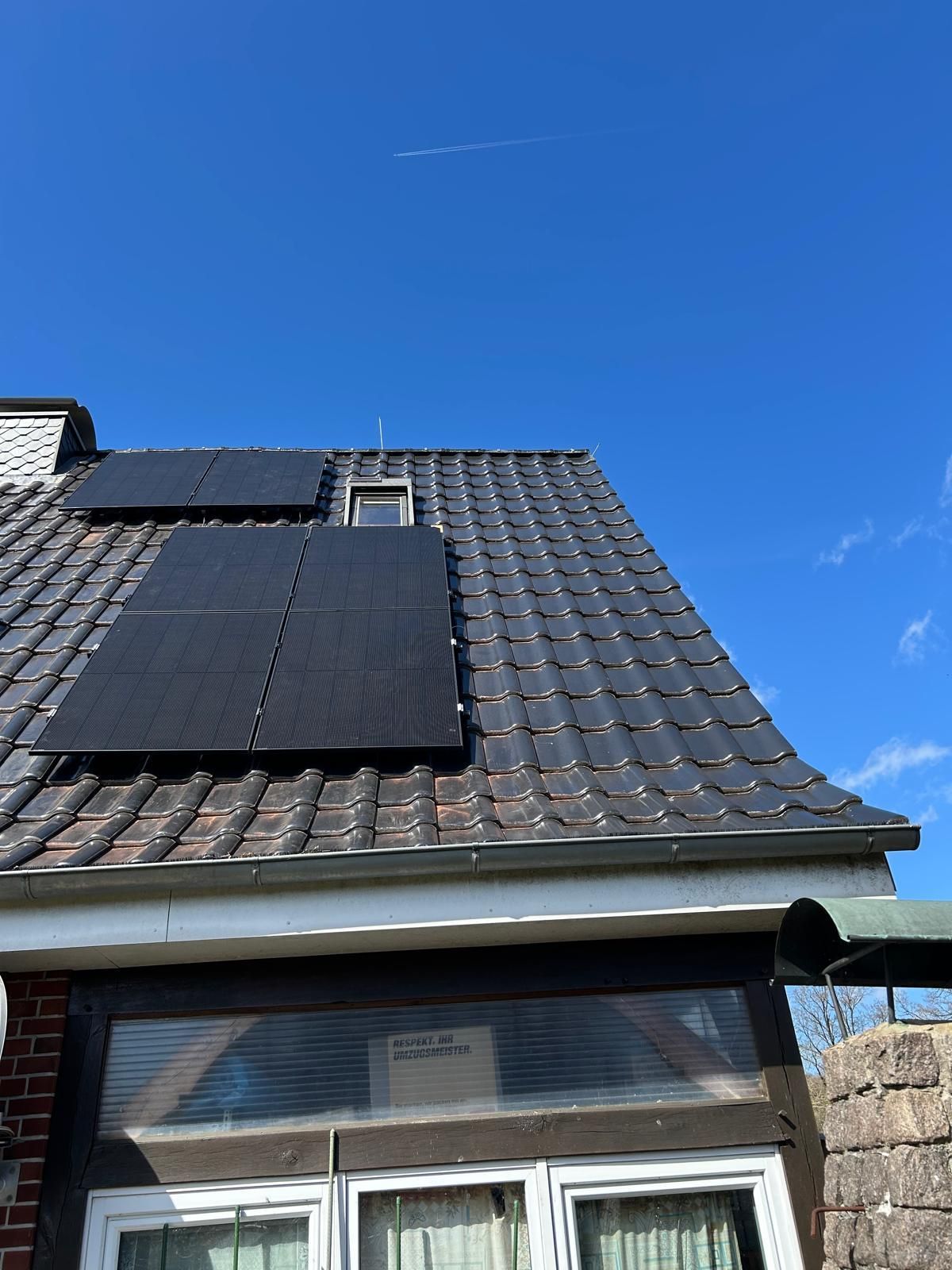 Hausdach mit dunklen Solarpaneelen unter klarem, blauem Himmel