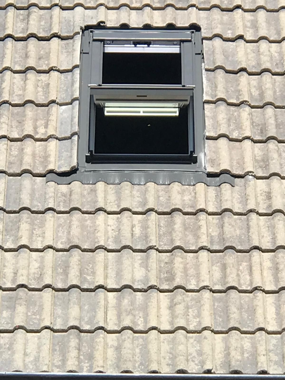Offenes Dachfenster mit schwarzem Rahmen auf einem grauen Ziegeldach