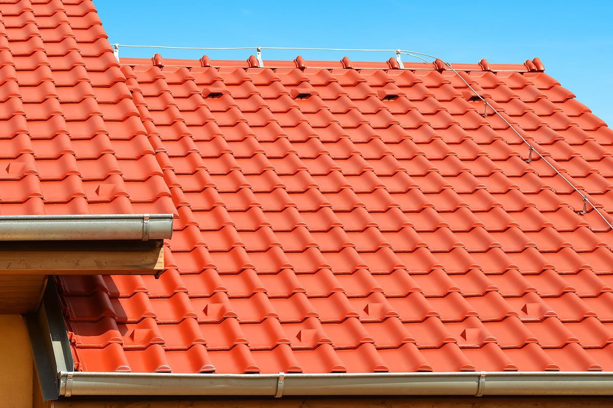 Rotes Ziegeldach vor klarem blauem Himmel, im Vordergrund Dachrinne und Dachkante
