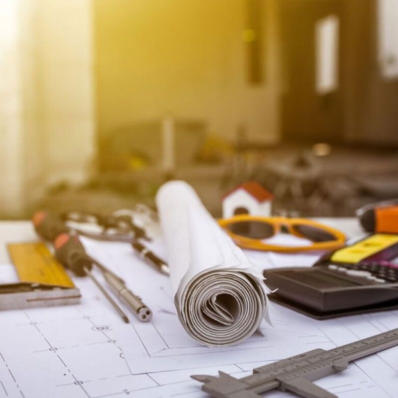 Herramientas de dibujo y planos enrollados sobre el escritorio de un arquitecto, con una regla y un teléfono inteligente delante.