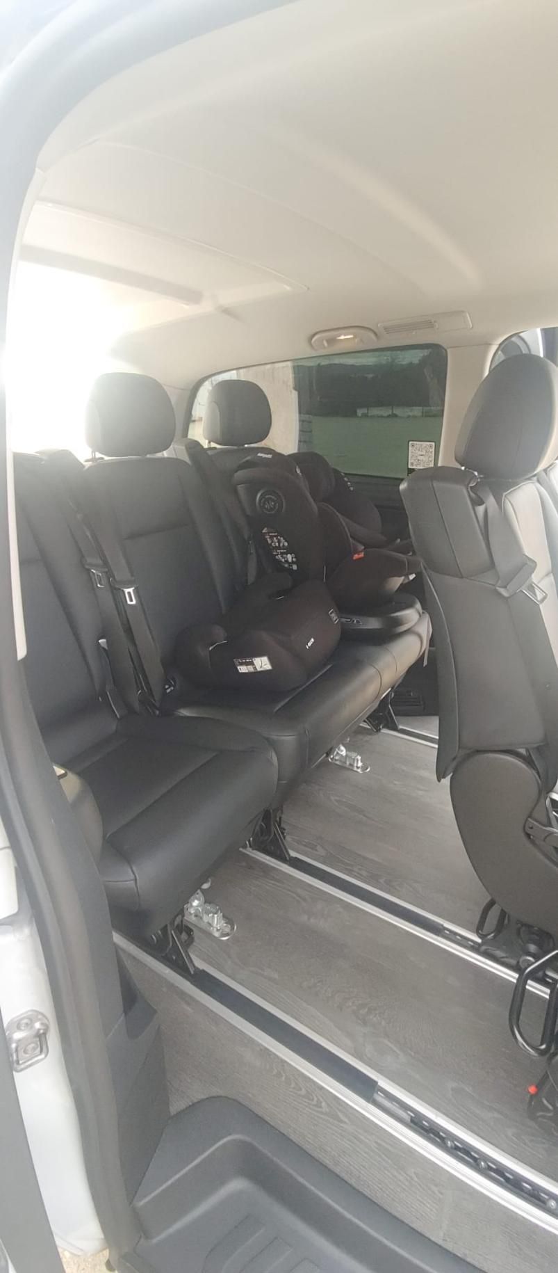 Vista interior de una camioneta con tres filas de asientos negros y bolsos en el medio.