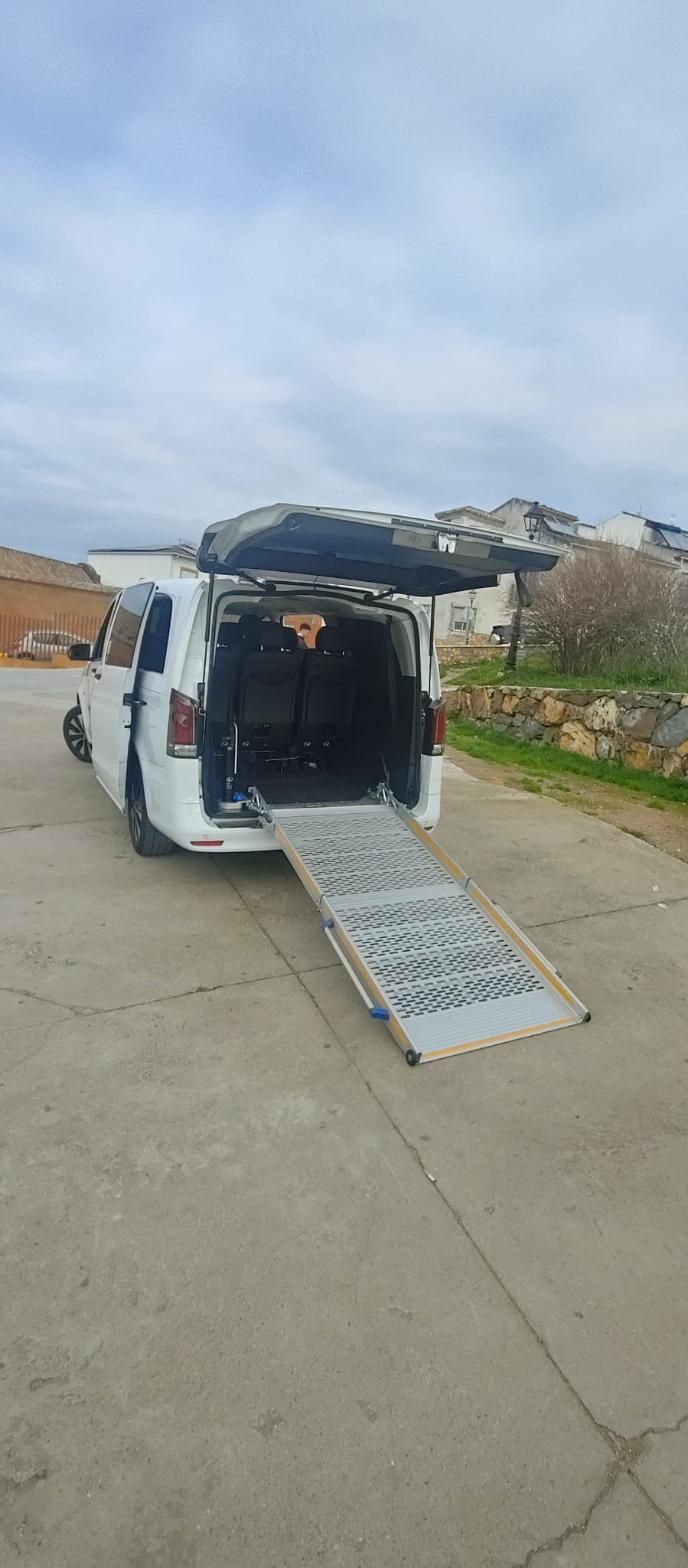 Furgoneta blanca con rampa extendida sobre hormigón, en el exterior. La parte trasera de la furgoneta está abierta.