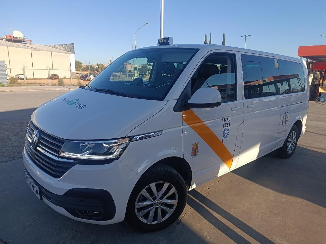 Taxi furgoneta Volkswagen de color blanco con franja naranja, aparcado al aire libre bajo la luz del sol.