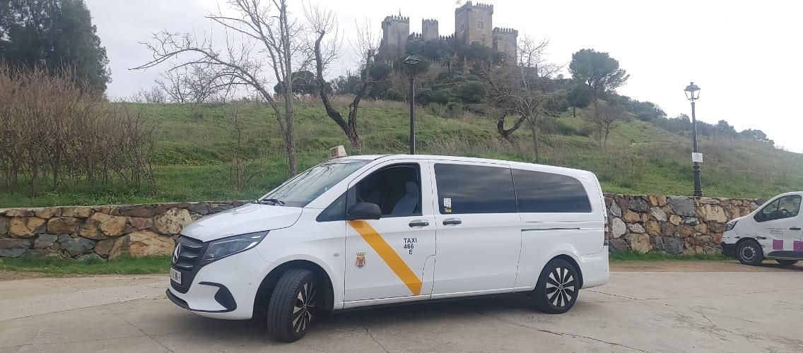 Furgoneta taxi blanca estacionada cerca de un castillo en un día nublado.