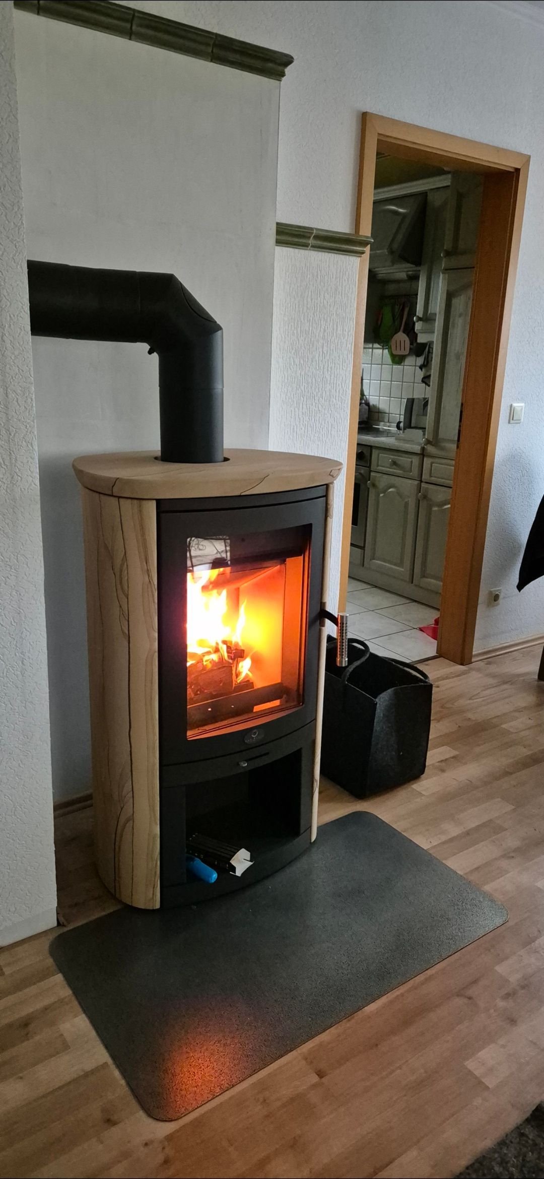 Ein Holzofen heizt einen gemütlichen Raum; neben einer offenen Tür und einem Hartholzboden sind Flammen zu sehen.