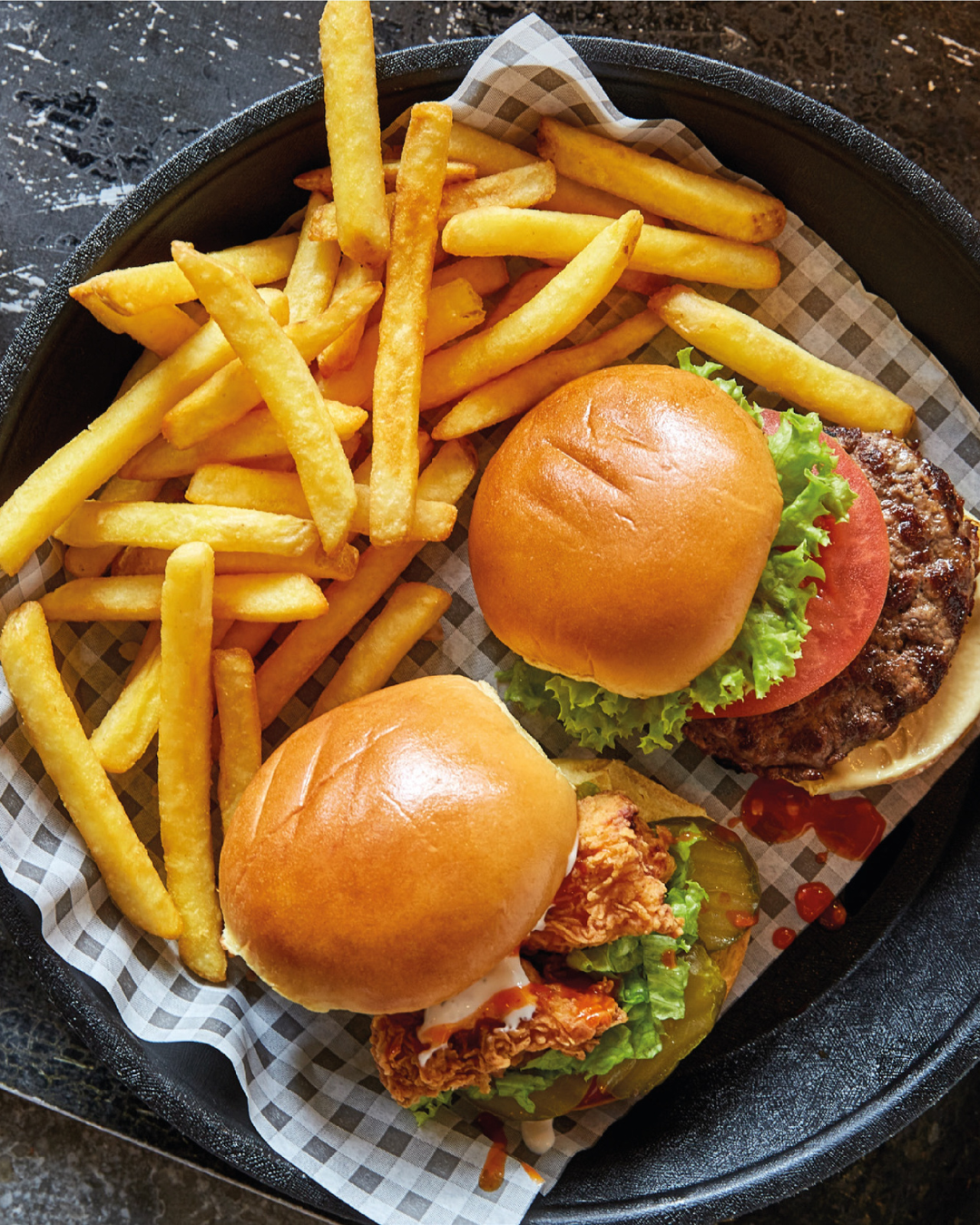 Dos hamburguesas y patatas fritas en un plato sobre una mesa.