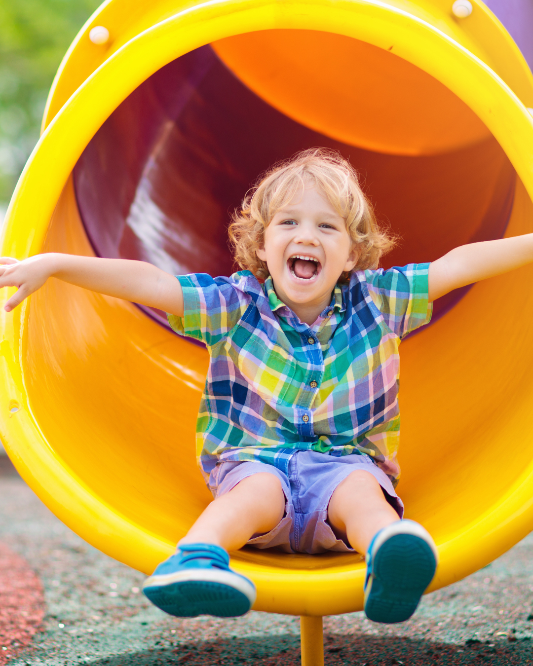 Un niño pequeño está sentado en un tobogán amarillo en un parque infantil.