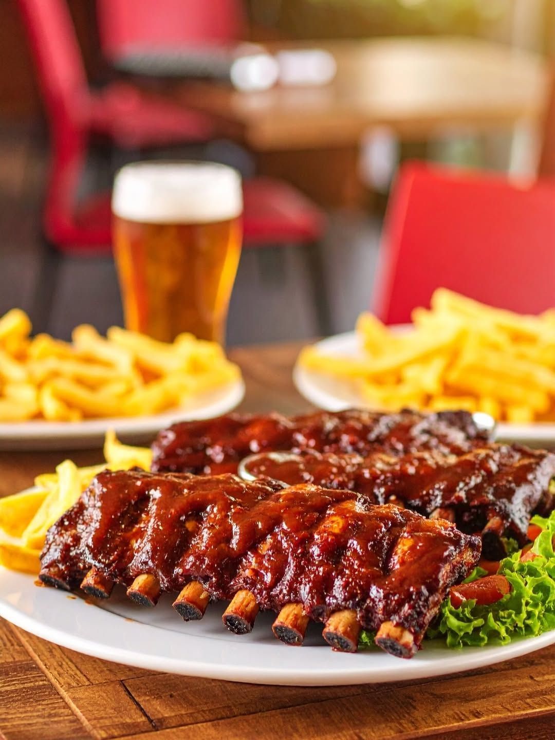 Un plato de costillas y patatas fritas en una mesa con un vaso de cerveza de fondo.