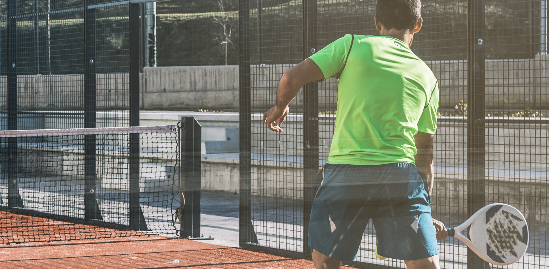 Un hombre con una camiseta verde está jugando al pádel en una cancha.