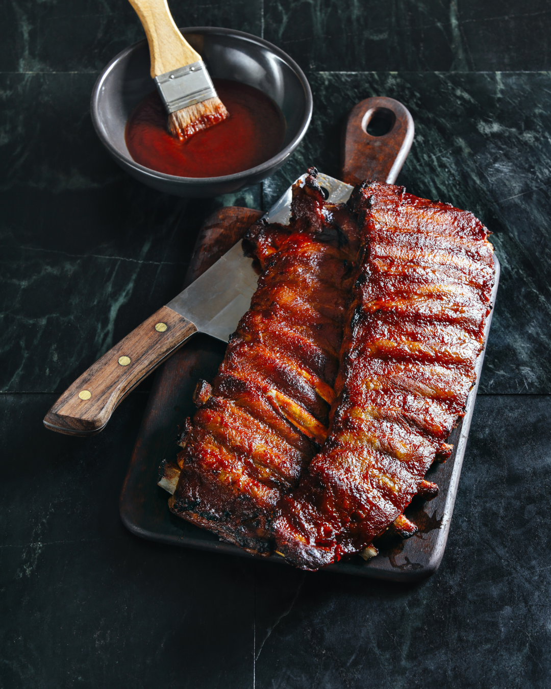 Una tabla de cortar cubierta con costillas y un tazón de salsa de barbacoa.