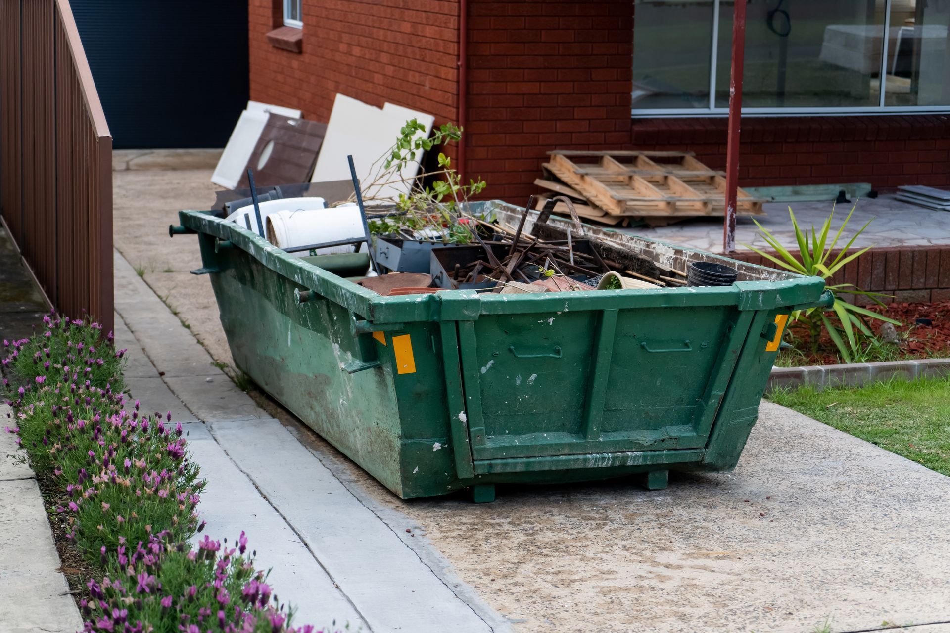 Benne verte avec divers déchets déposée devant une maison