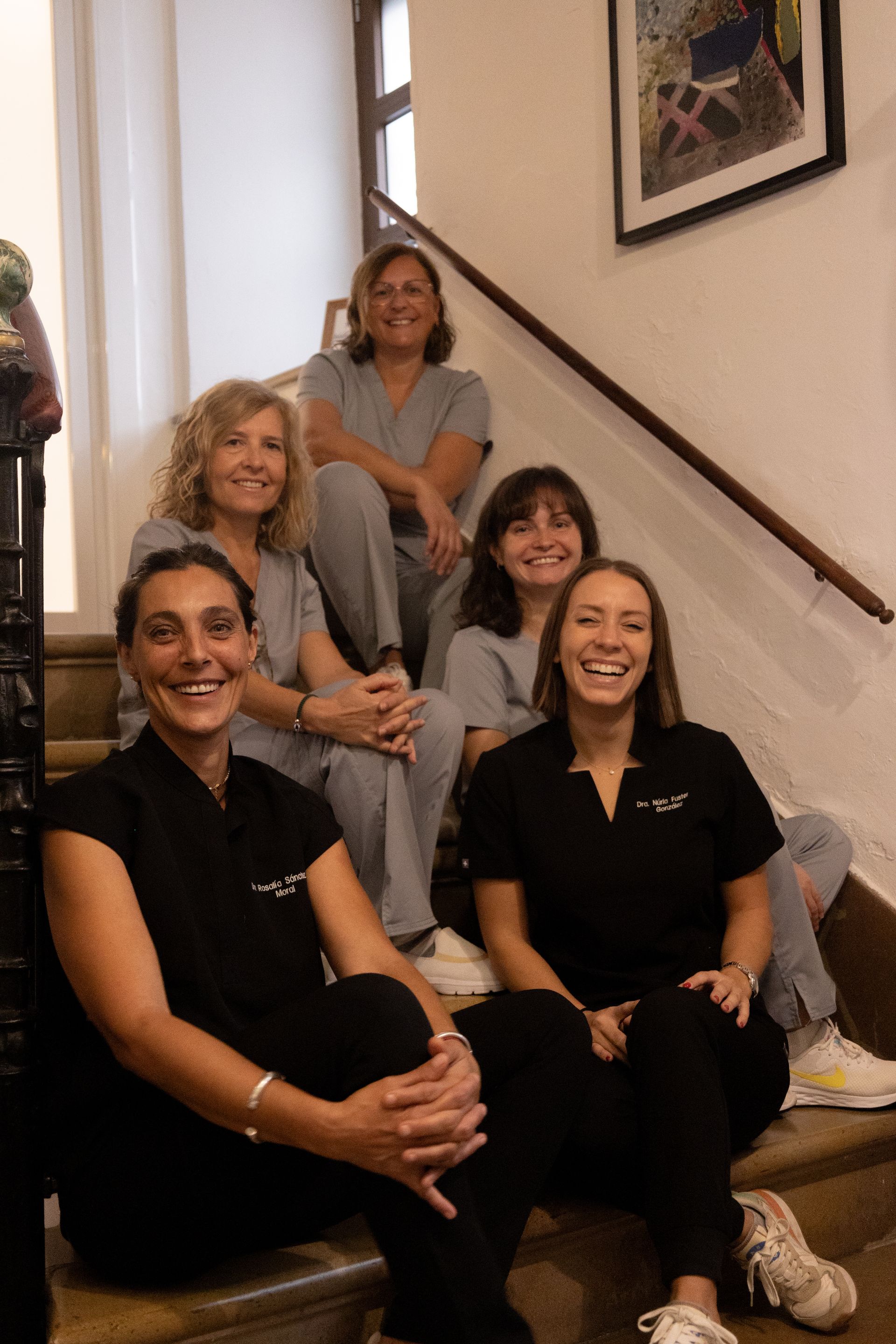 Seis personas con uniforme médico, sonrientes, posan en las escaleras. Tonos cálidos y luz natural.