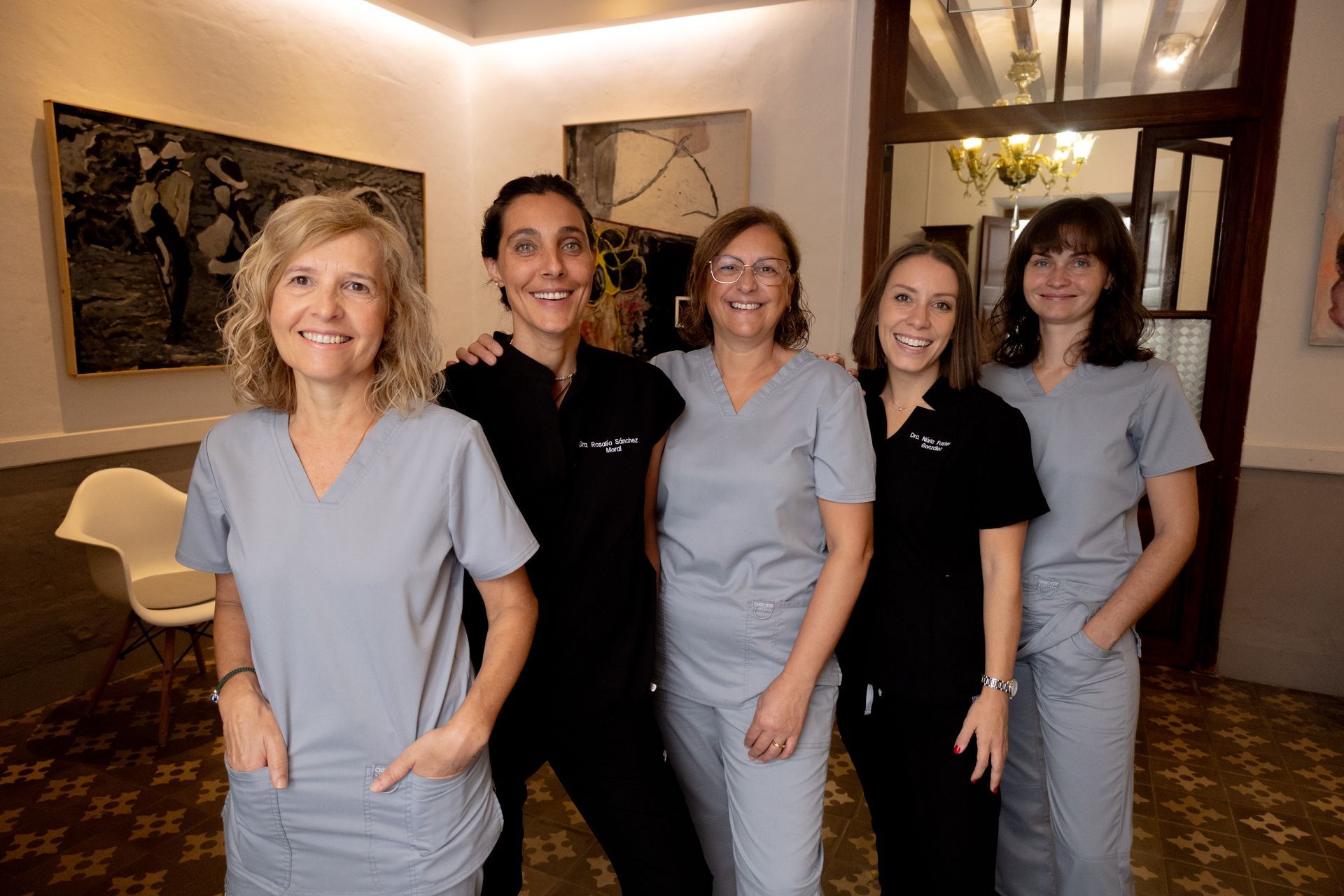 Cinco personas con uniformes médicos posan en una habitación. Dos mujeres vestidas de negro 