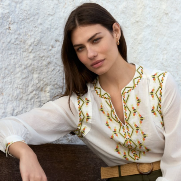 Una mujer que lleva una camisa blanca con bordados verdes y naranjas.