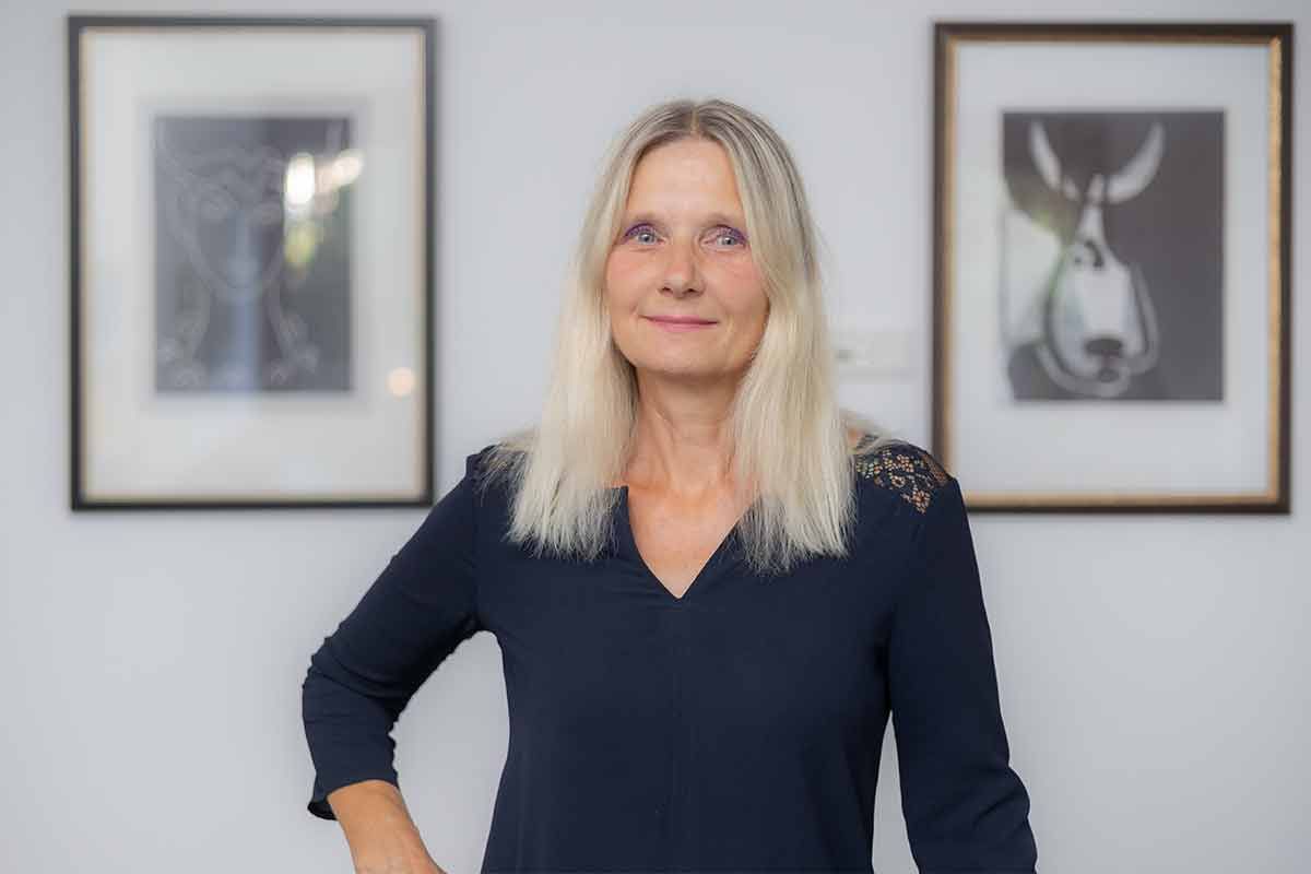 Eine Frau steht vor zwei gerahmten Bildern an einer Wand.