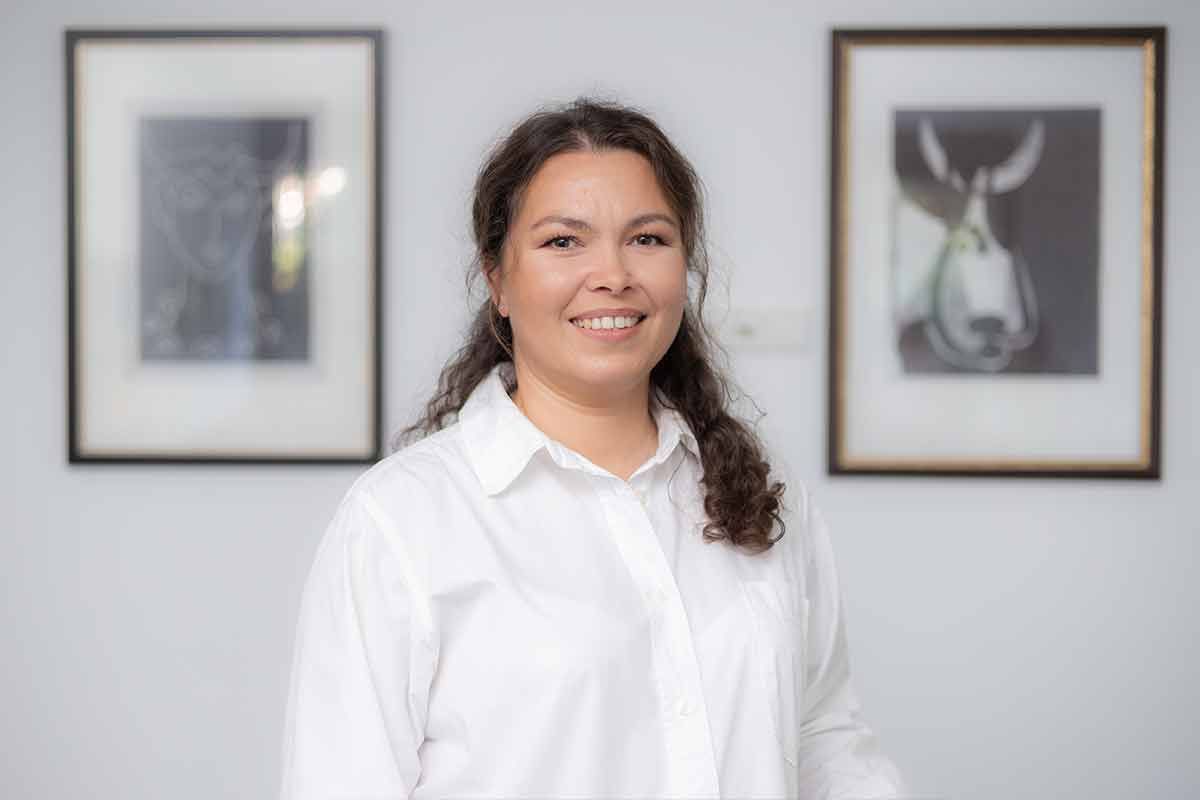 Eine Frau in einem weißen Hemd steht vor zwei gerahmten Bildern.