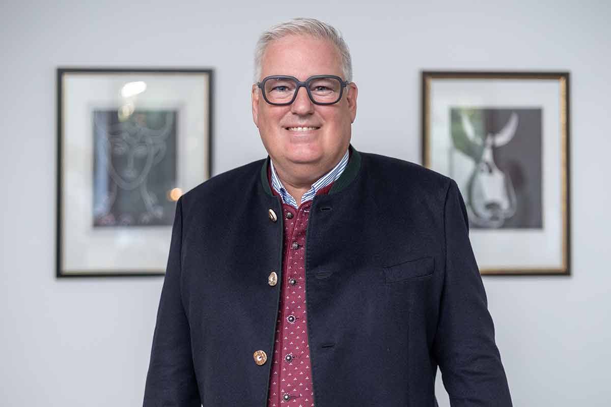 Ein Mann mit Brille und Jacke steht vor zwei gerahmten Bildern.