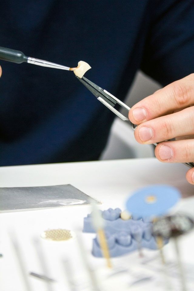 Des mains utilisent un outil pour travailler sur un modèle dentaire avec des dents artificielles.