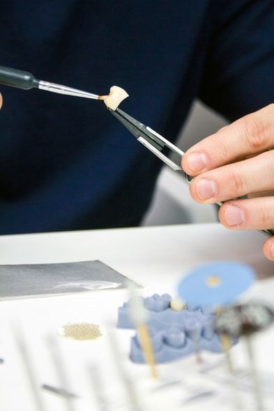 Des mains utilisent un outil pour travailler sur un modèle dentaire avec des dents artificielles.