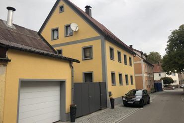 Großes Haus mit gelber Fassade mit schwarzem Auto davor
