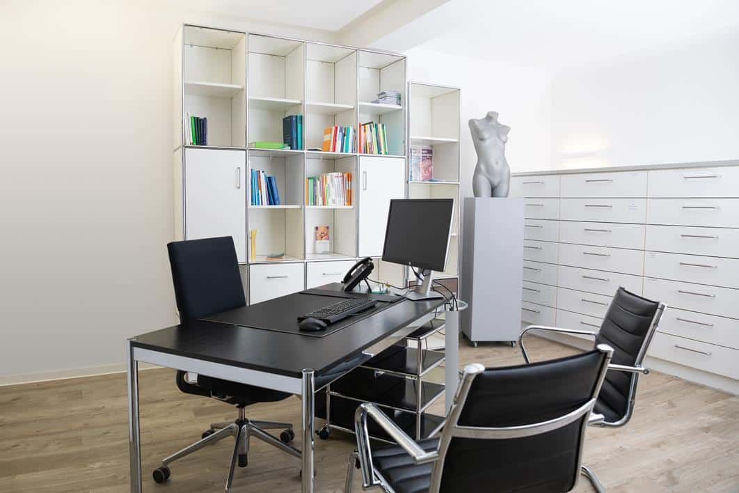 Modernes Büro mit schwarzem Schreibtisch, Laptop, Stuhl, weißen Regalen und Aktenschränken