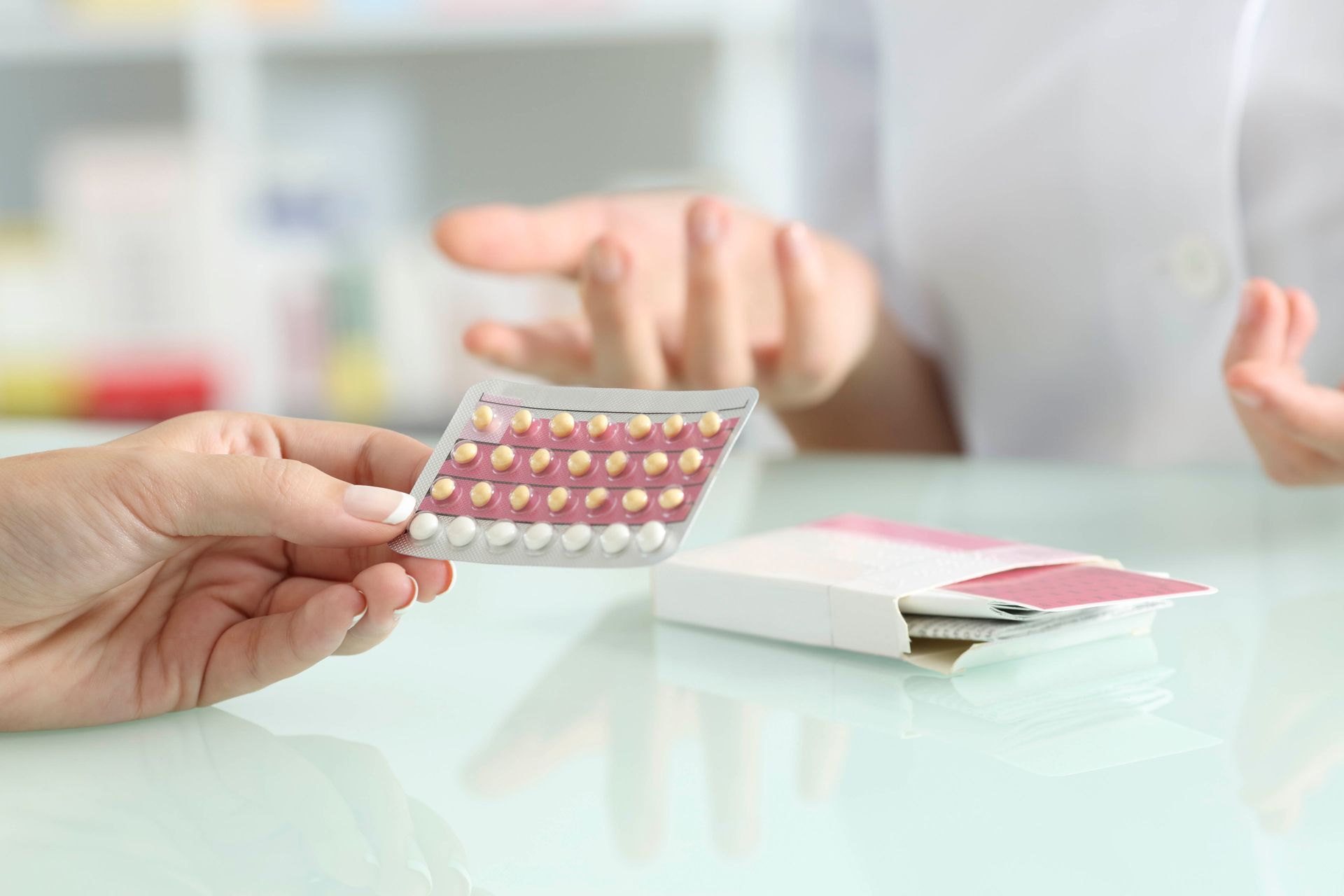 Eine Hand hält eine Blisterpackung Tabletten über einen Tisch hinweg auf eine verschwommene Person zu