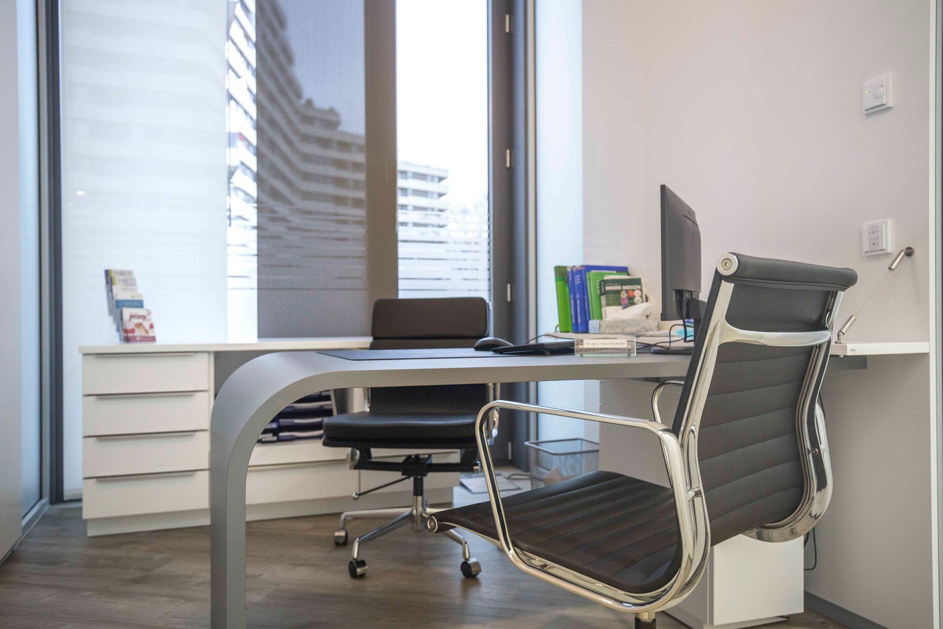 Modernes Büro mit weißem Schreibtisch, schwarzem Stuhl, Computermonitor und großem Fensterblick