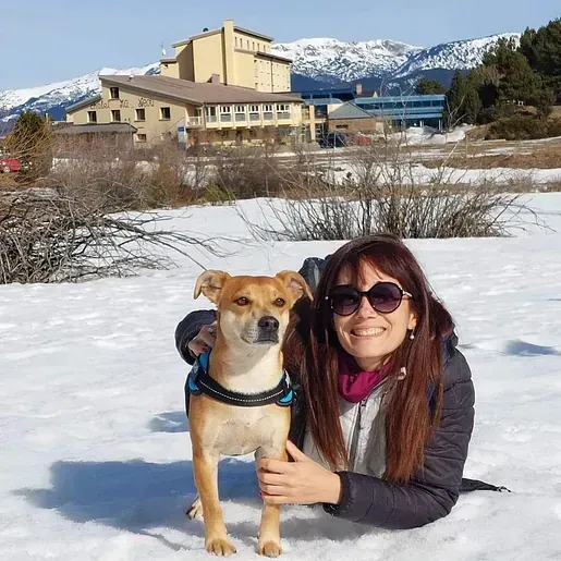 Una mujer está tumbada en la nieve con su perro.