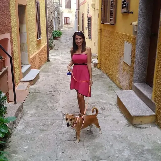 Una mujer con un vestido rosa pasea a un perro con correa.