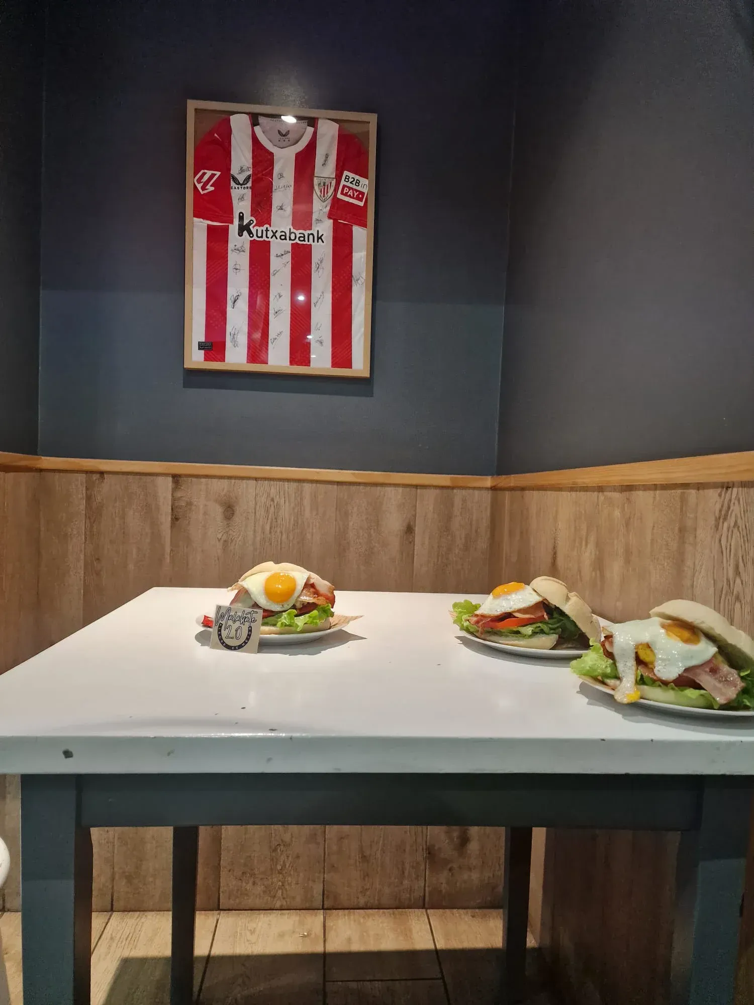 Hay dos sándwiches sobre una mesa frente a una camiseta enmarcada.