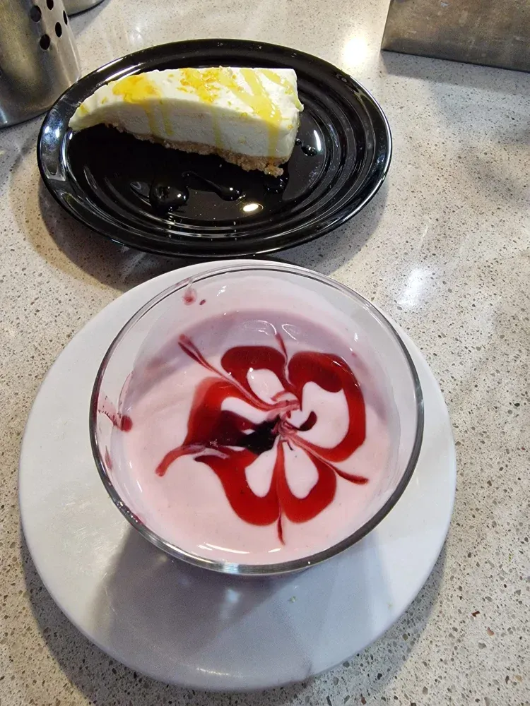 En un plato hay una rebanada de tarta de queso junto a un bol de yogur.