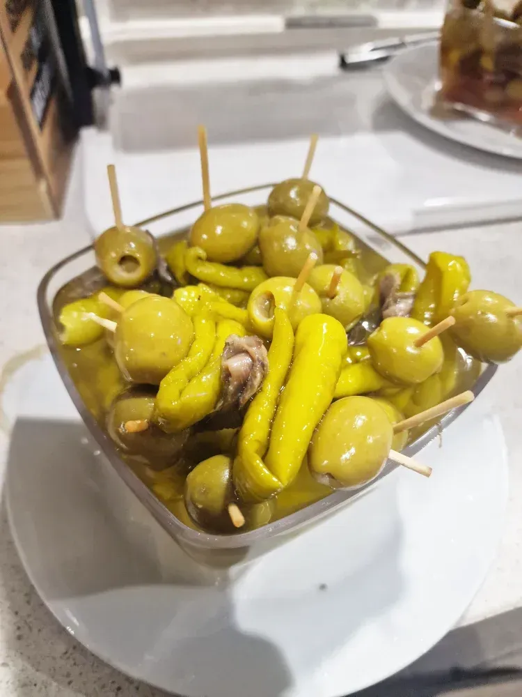 Un bol de aceitunas encurtidas y pimientos en palitos en un plato blanco.