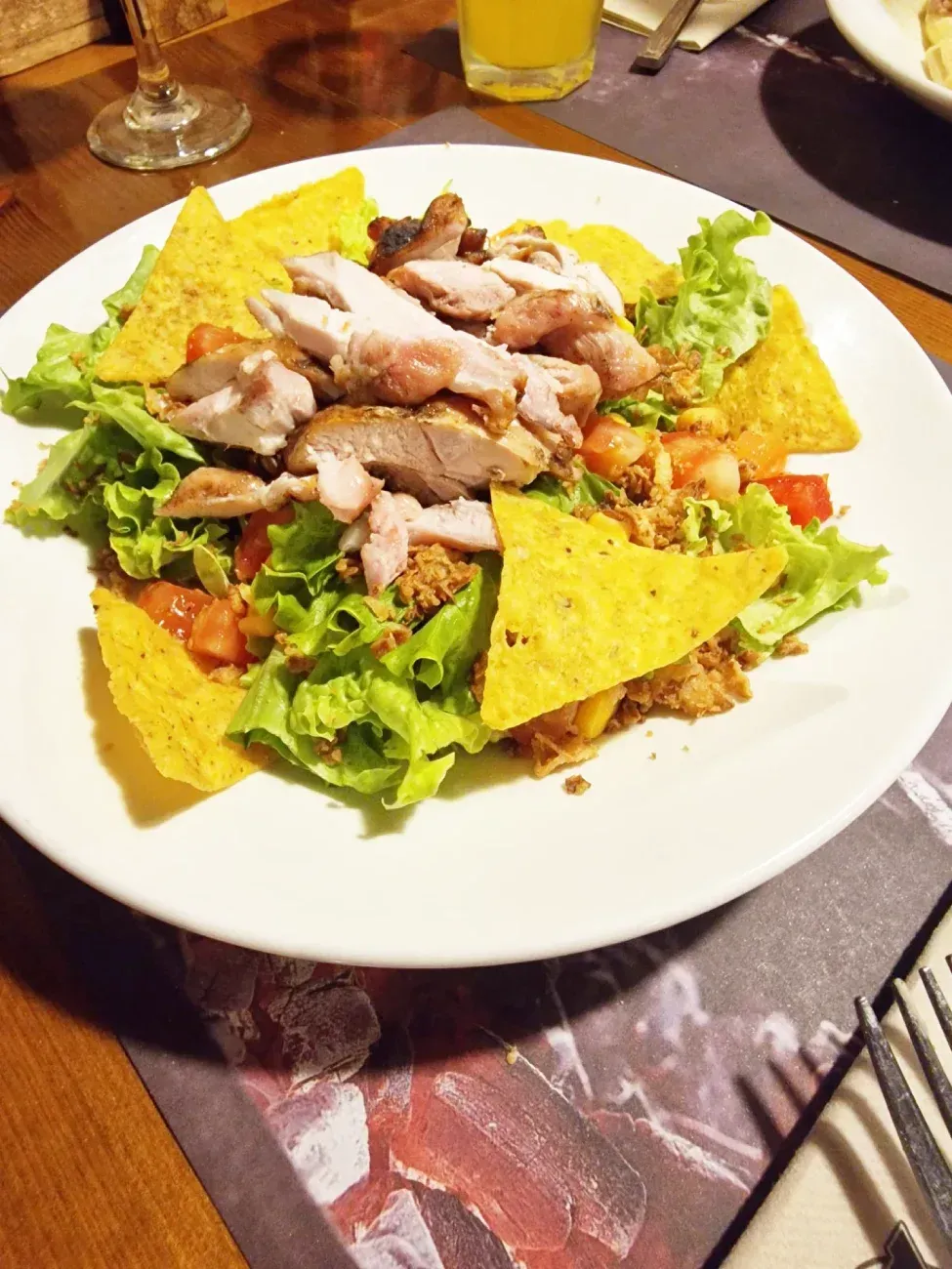 Un plato blanco cubierto con ensalada y tortillas chips sobre una mesa.