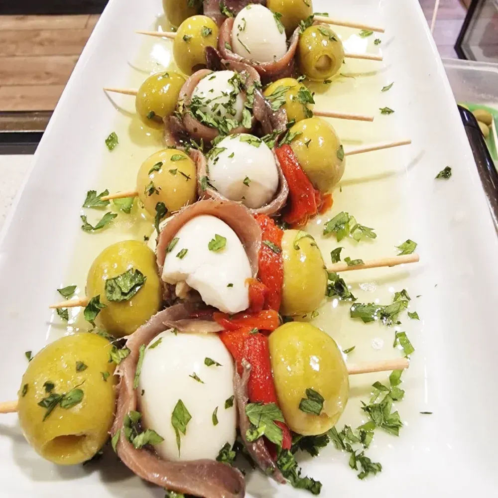 Un plato blanco cubierto con aceitunas, anchoas y pimientos.