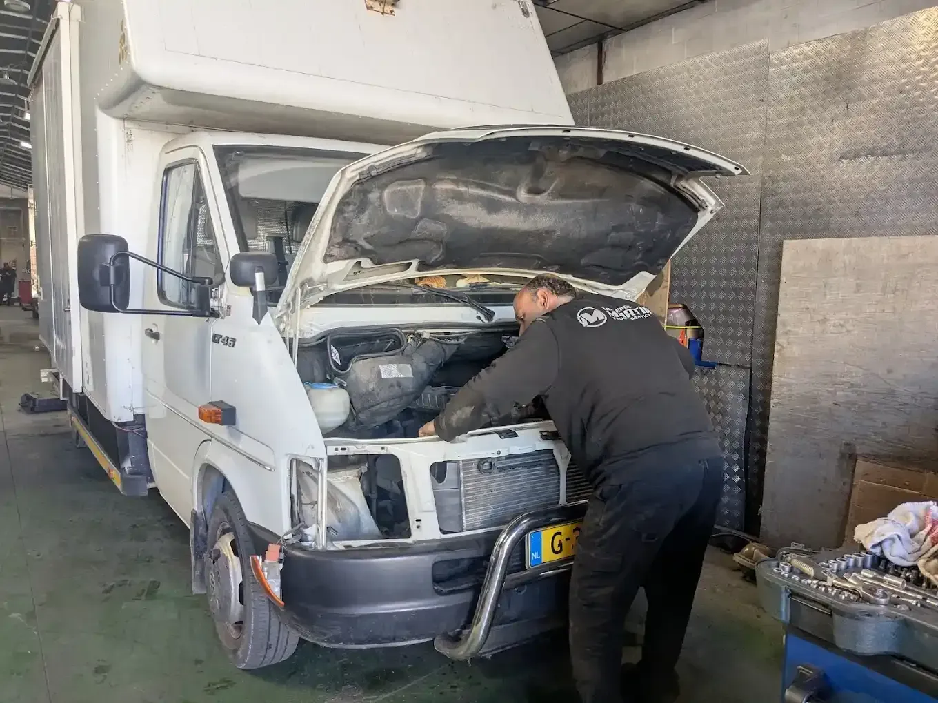 Mecánico trabajando en el motor de un camión de caja blanca dentro de un garaje.