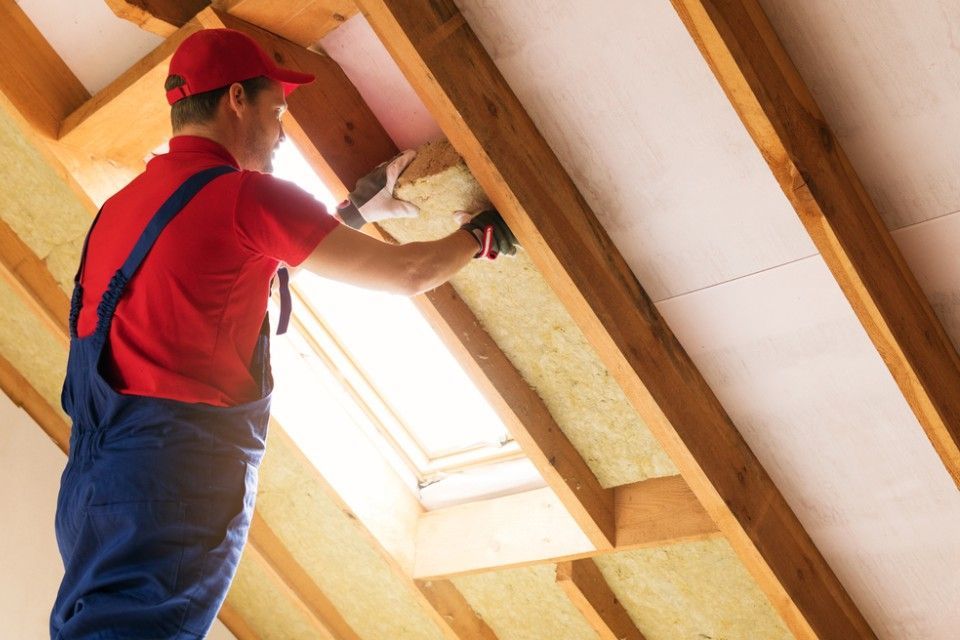 RW Dach GmbH & Co. KG – ein Dachdecker im Inneren eines Dachgeschosses installiert Isoliermaterial zwischen den Dachbalken