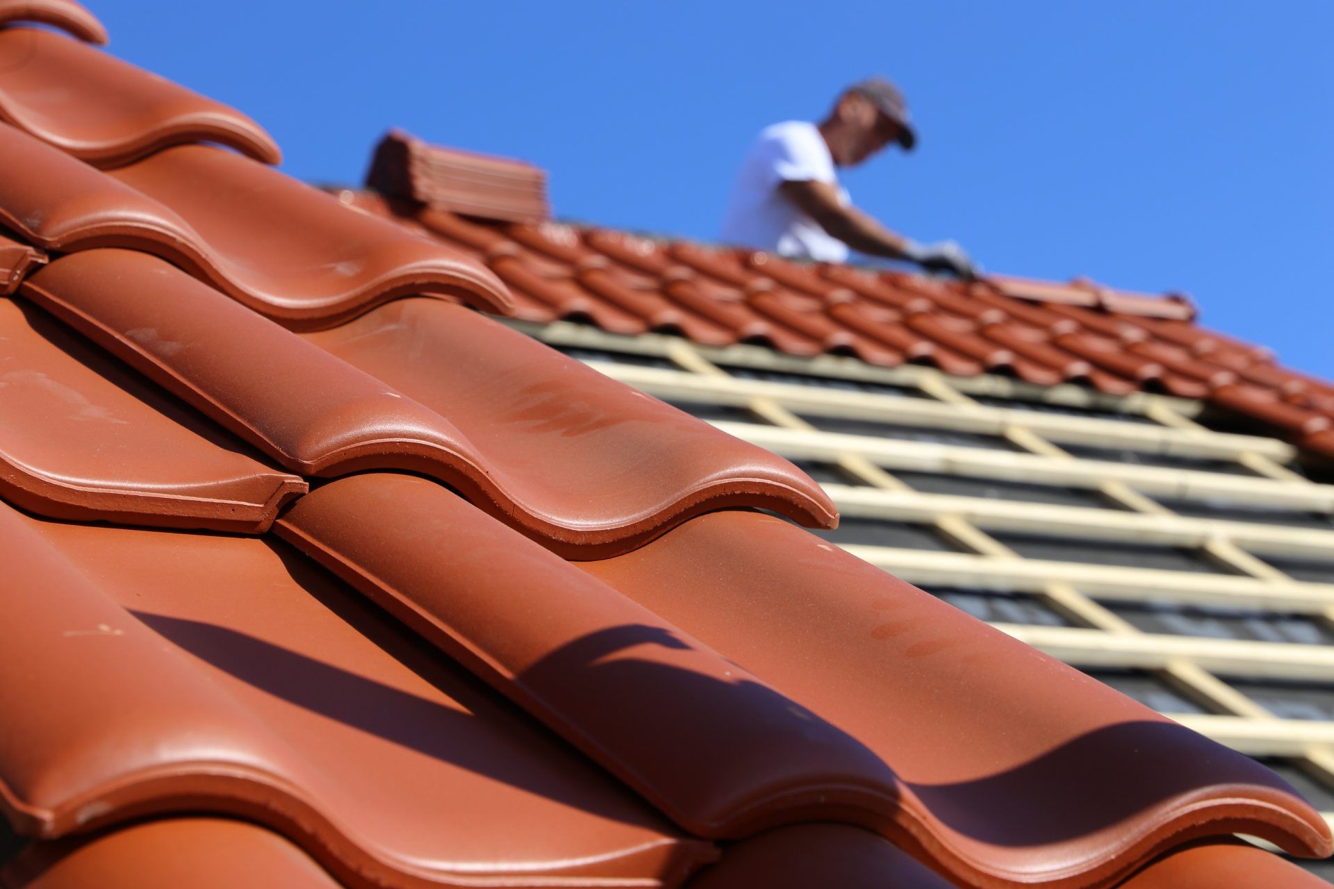 RW Dach GmbH & Co. KG – Dachziegel im Fokus, im Hintergrund ein Dachdecker beim Eindecken eines Daches