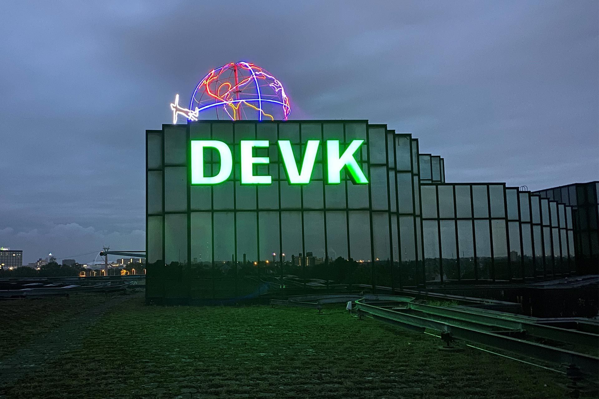 Gebäude der DEVK mit Logo-Leuchtreklame und einer Weltkugel aus Neonleuchtgittern auf dem Dach