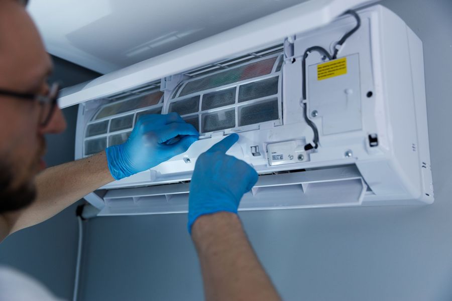 Un homme portant des gants bleus nettoie le filtre d'un climatiseur ; à l'intérieur.