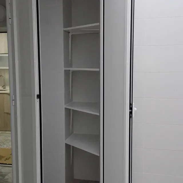 Un armario blanco con estantes y una puerta en una habitación.