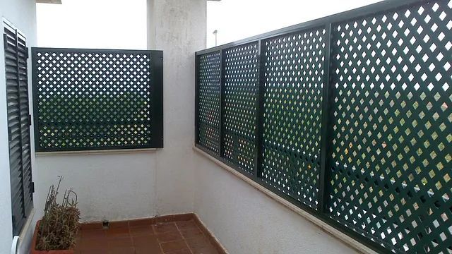 Un balcón con celosía verde y contraventanas.