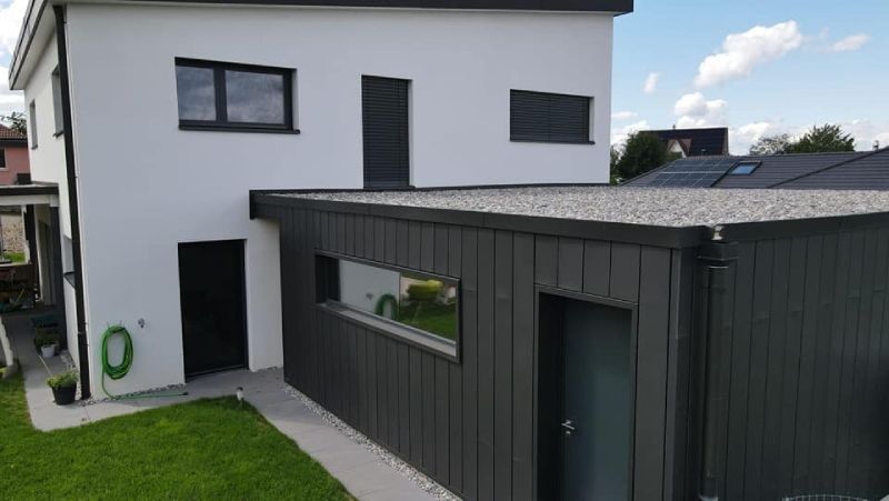 Une maison blanche avec un garage noir attenant.