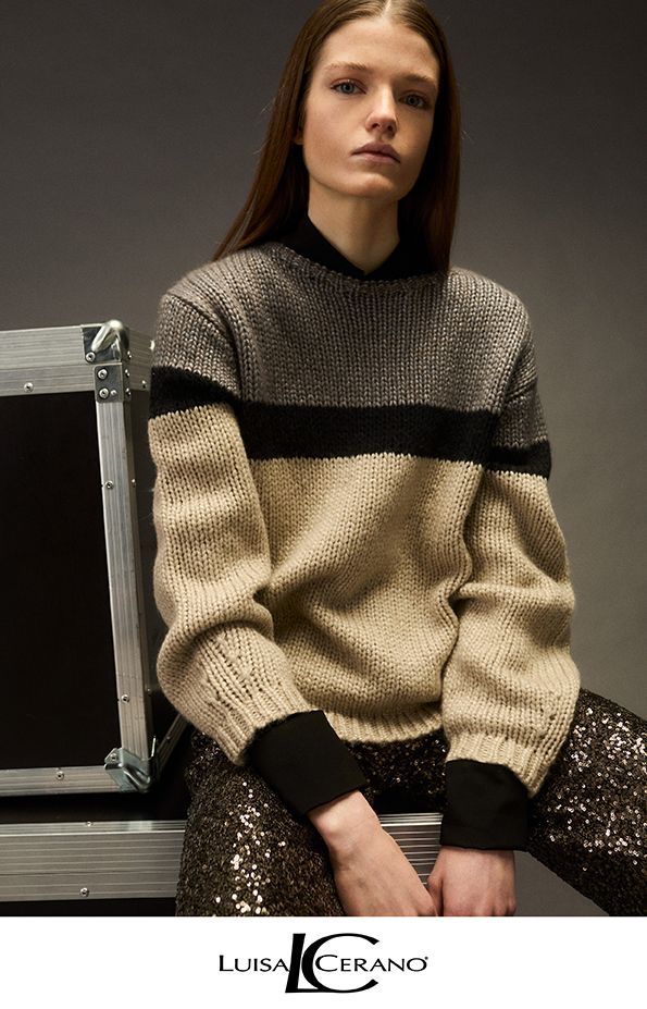 Frau in einem farblich abgesetzten Pullover und Paillettenhose, sitzt auf einem Koffer, Studio-Kulisse.