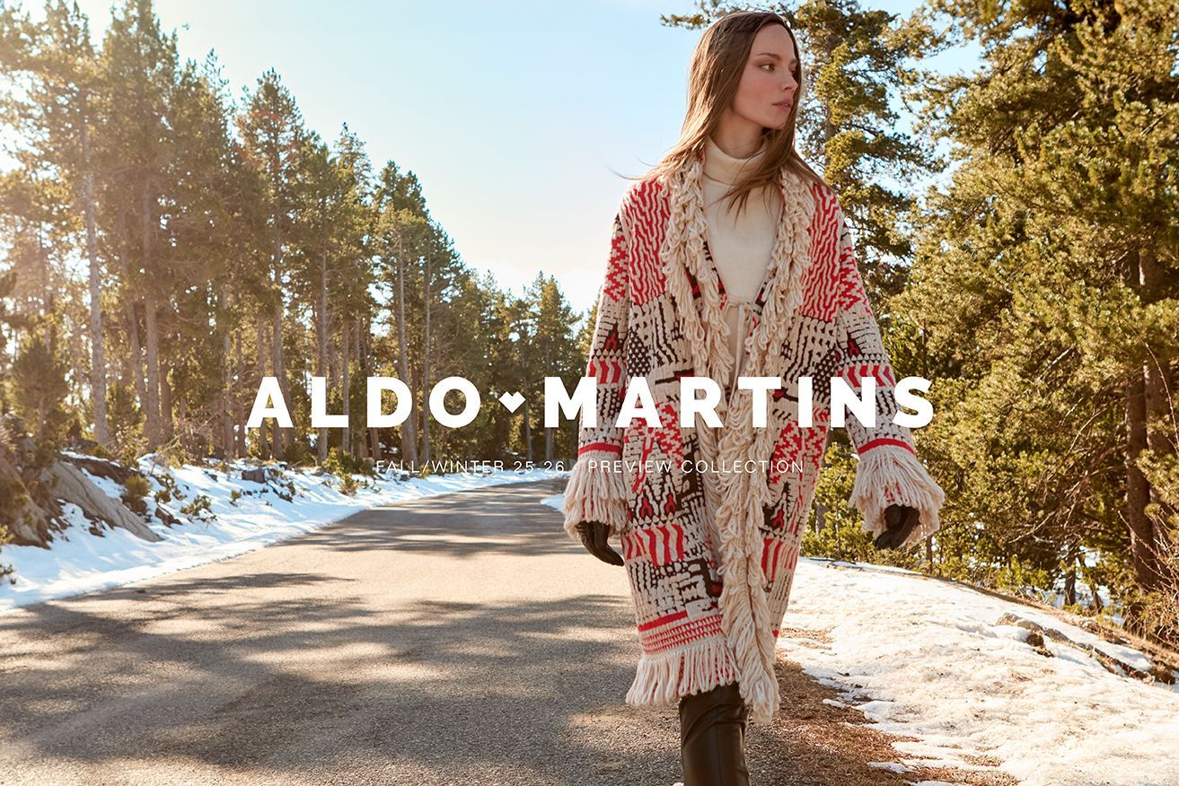 Frau in gemustertem Mantel geht auf einer schneebedeckten Straße, Logo „ALDO MARTINS“ in der Mitte.