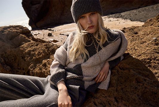 Frau mit Strickmütze und kariertem Schal liegt auf Felsen am Meer