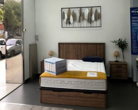 Un dormitorio moderno con una cama de madera, ropa de cama amarilla, mesitas de noche y cuadros en la pared junto a una ventana.
