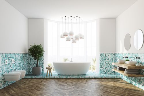 Eine weiße Badewanne in einem hellen Raum mit blauen Mosaikfliesen an der Wand und einem kleinen Baum in der Ecke.